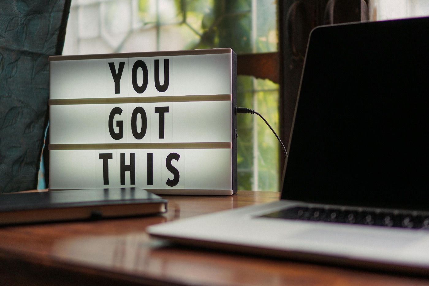 A laptop, notebook and a sign on the table. Sign says 