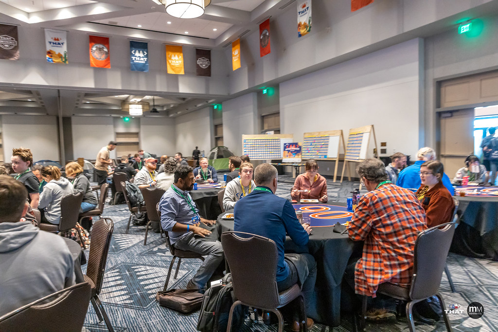 Lots of people sitting around tables in the conference hall, chatting and eating a meal together.