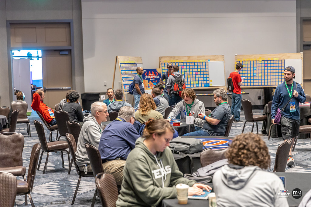 Several people gathered around tables in the conference hall, chatting about various open-space topics.