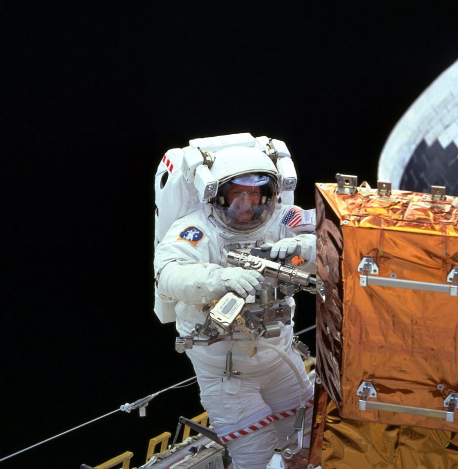 Astronaut Claude Nicollet uses the Pistol Grip Tool on a storage container during the Hubble 3A servicing mission